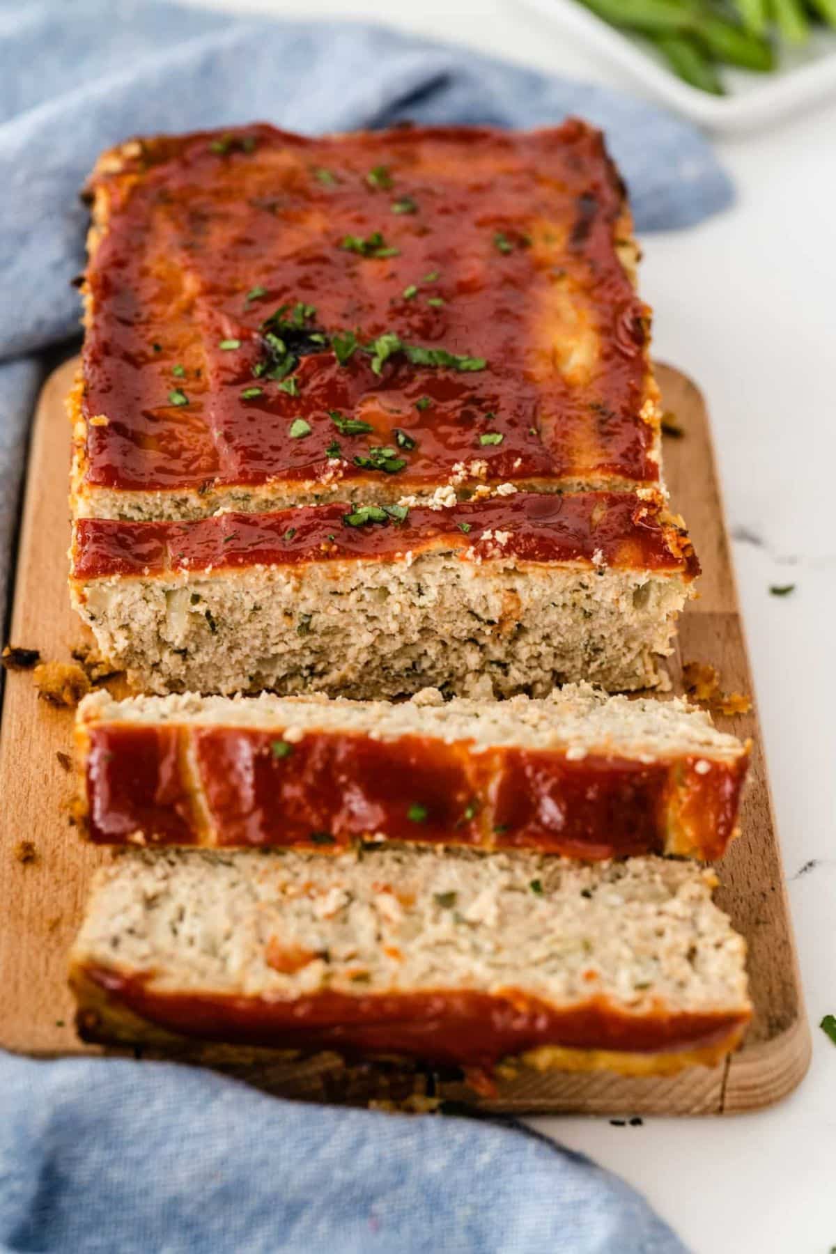 Partially sliced Chicken Meatloaf Without Breadcrumbs on a wooden cutting board.