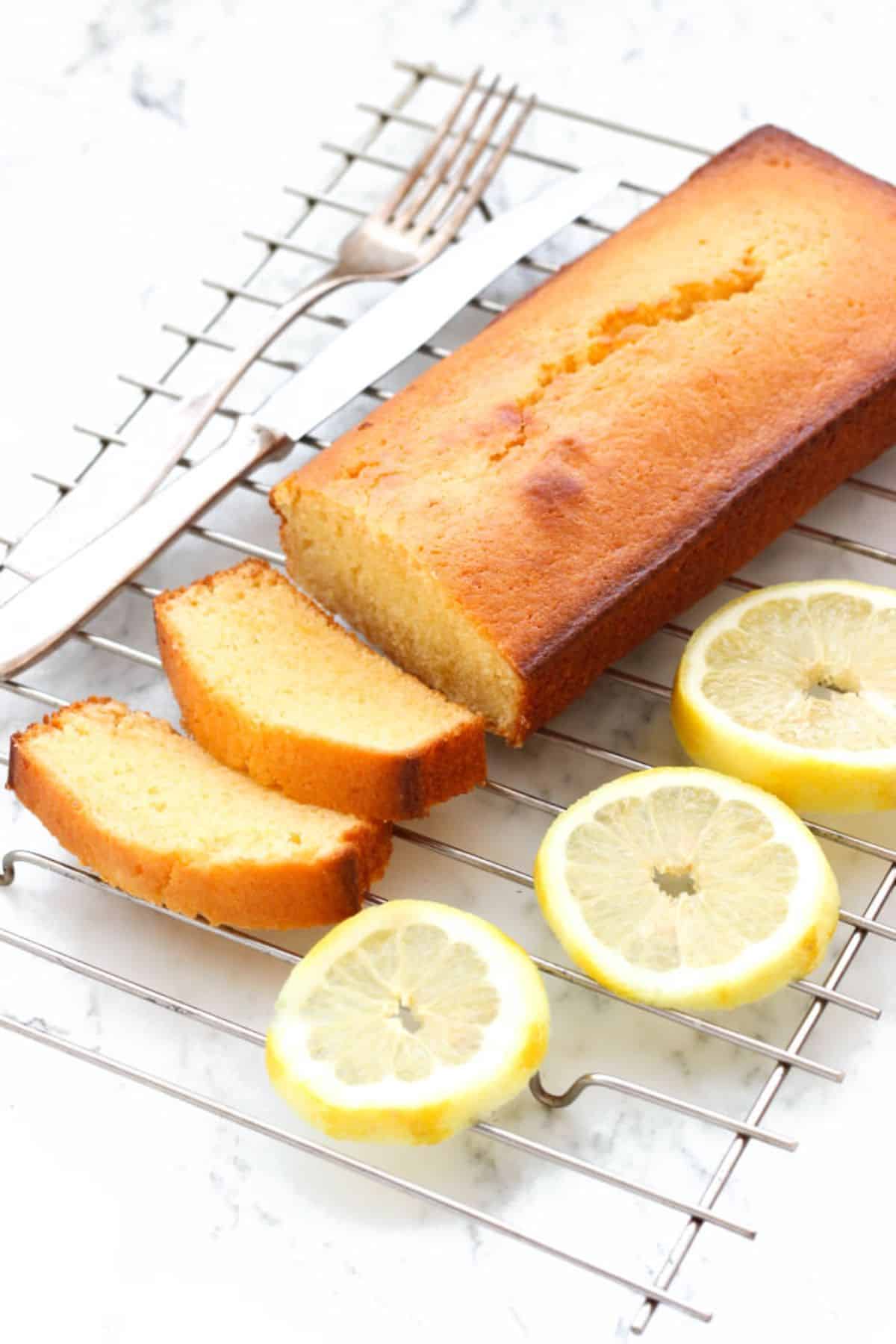 Easy Lemon Yogurt Cake (Gluten-free) on a resting grid with a cutlery and pieces of lemon.
