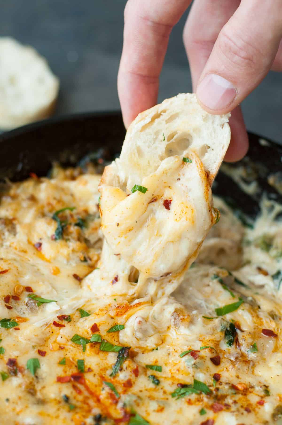 Baked Seafood Dip in a black bowl scooped by a piece of bread.