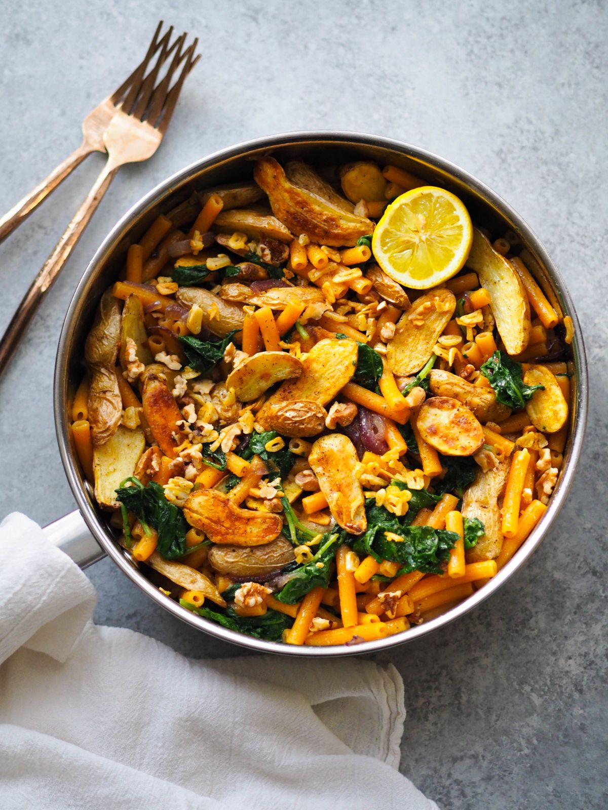 Lentil Pasta with Roasted Fingerlings, Baby Kale, and Crispy Garlic in a skillet.