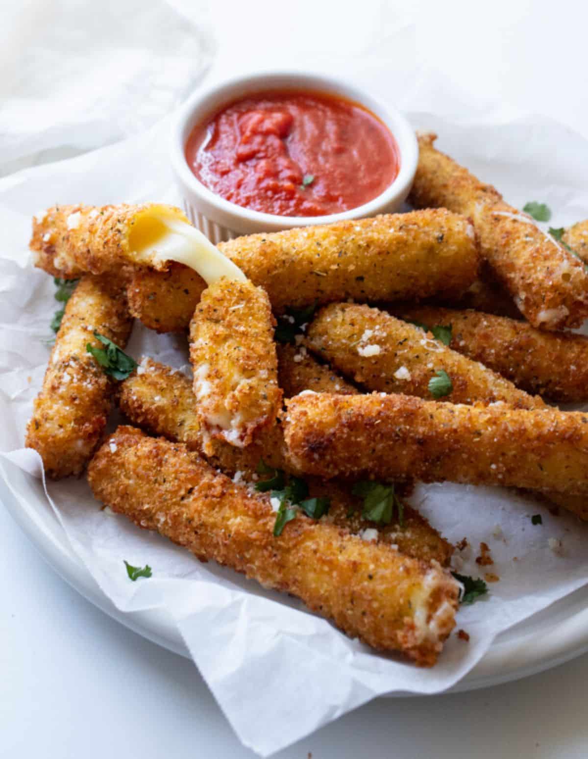 Gluten-Free Mozzarella Sticks with a dip in bowl on a plate.