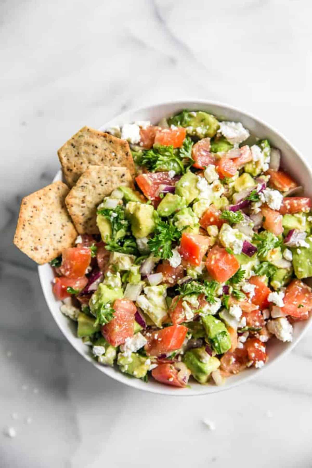 Seriously Addicting Avocado Feta Dip with crackers in a white bowl.