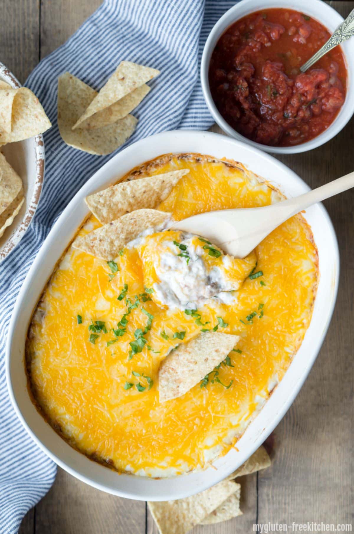 Cheesy Bean Dip with a wooden spatula and chips in a white bowl.