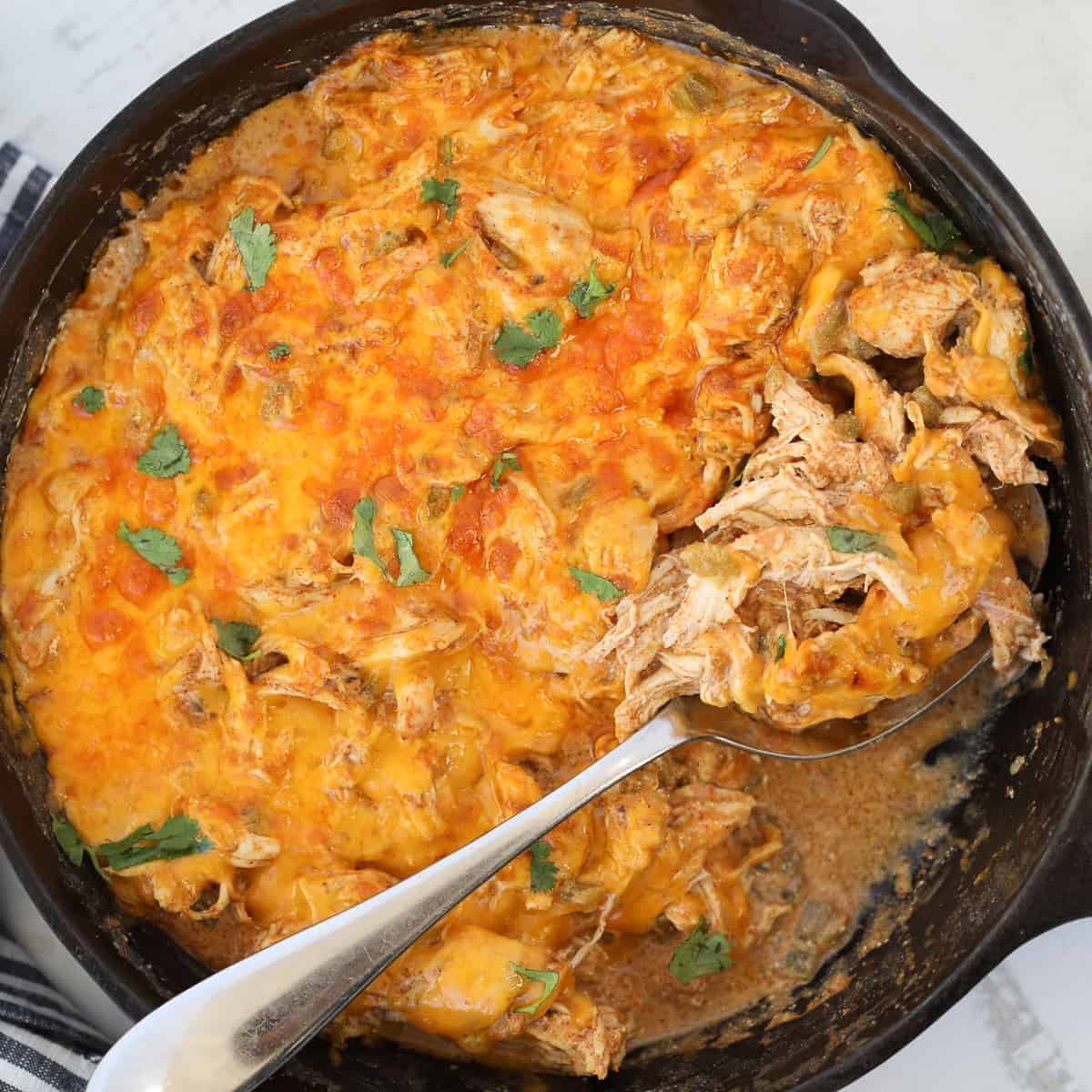 Sour Cream Chicken Enchilada in a black casserole with a spoon.