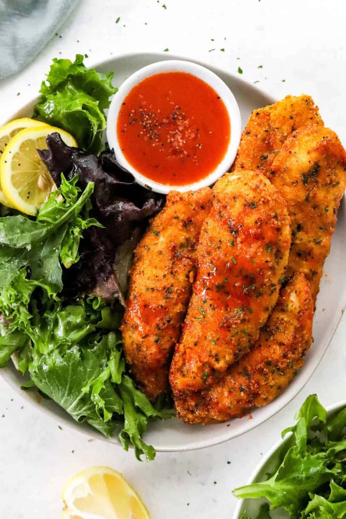 Air Fryer Chicken Tenders with veggies and a bowl of sauce on a white plate.