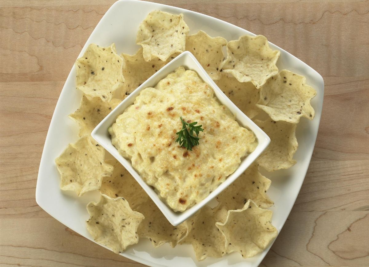 Baked Parmesan Onion Dip in a white bowl on a white tray with chips.
