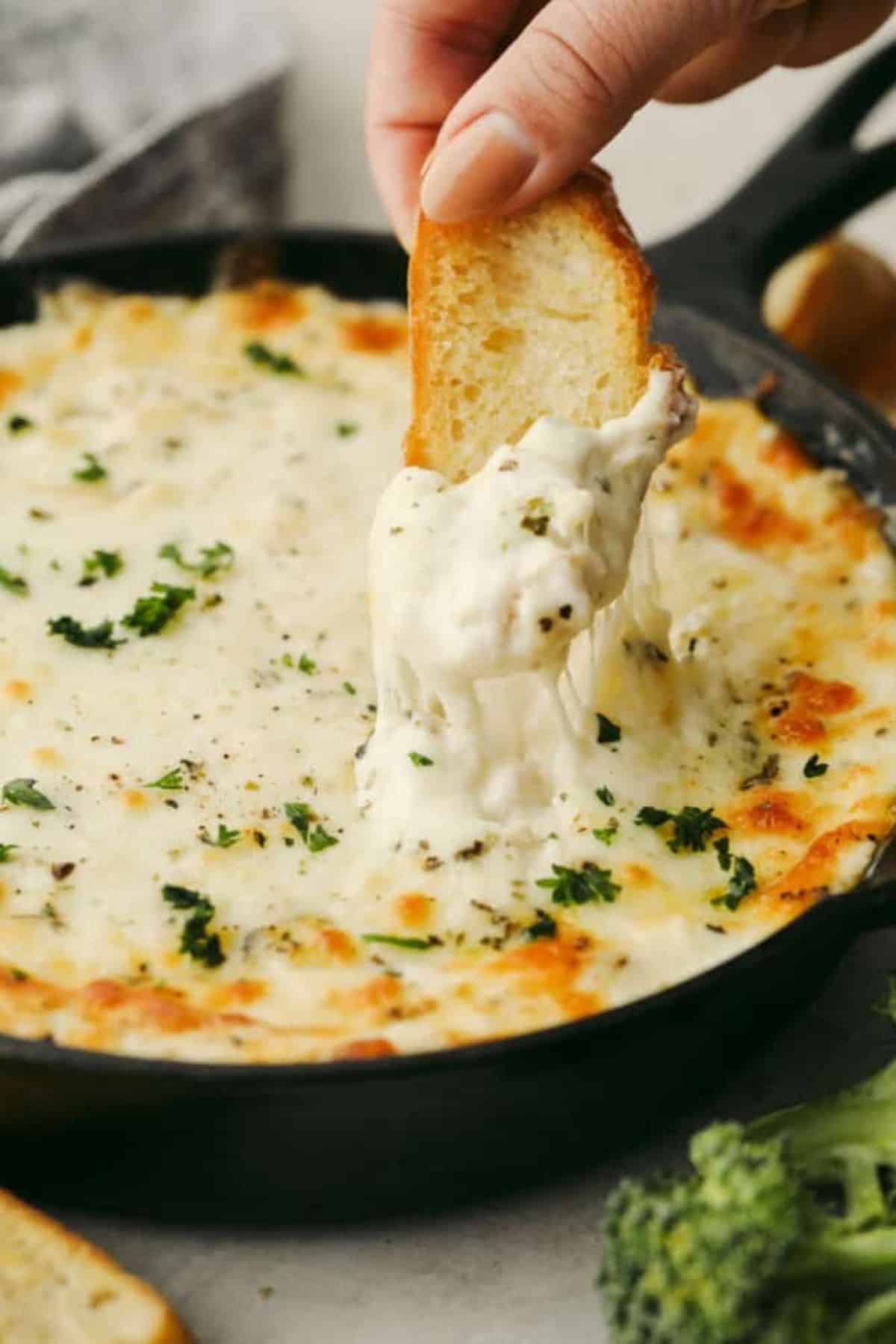 Chicken Alfredo Dip in a black pan scooped with a piece of bread.