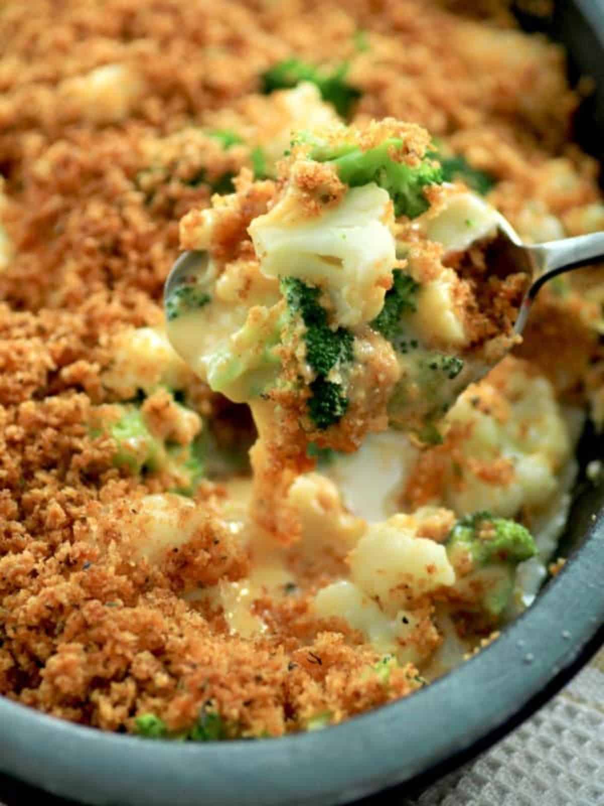 Broccoli Cauliflower Cheese Bake in a blue casserole scooped by a spoon.