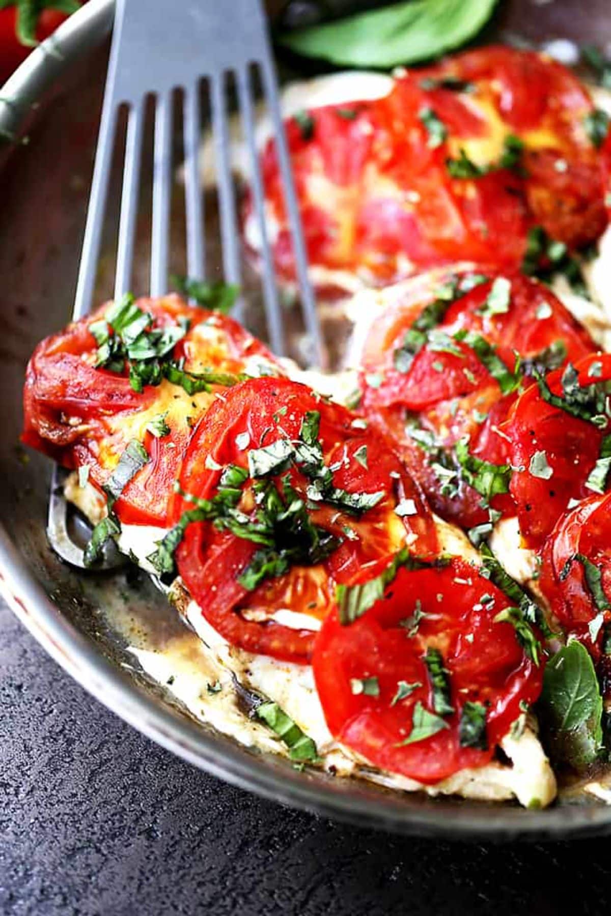 Caprese Skillet Chicken with a spatula in a black pan.