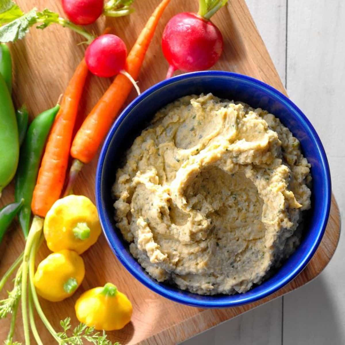 Classic Hummus in a blue bowl on a wooden cutting board with veggies.