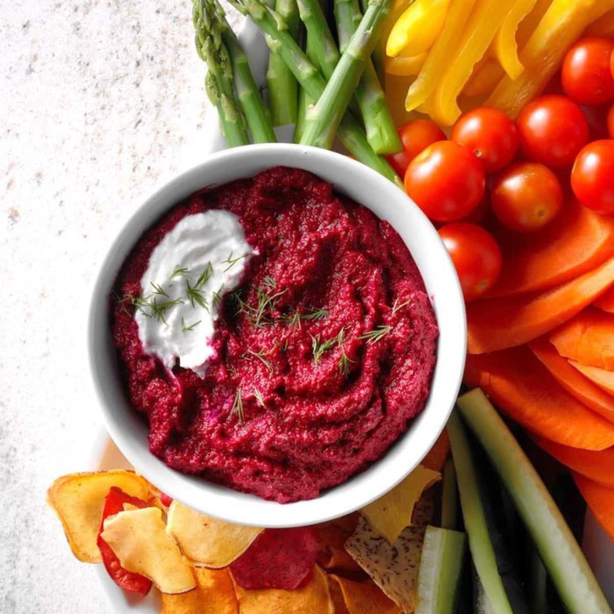 Roasted Beetroot and Garlic Hummus in a white bowl on a table with sliced veggies.