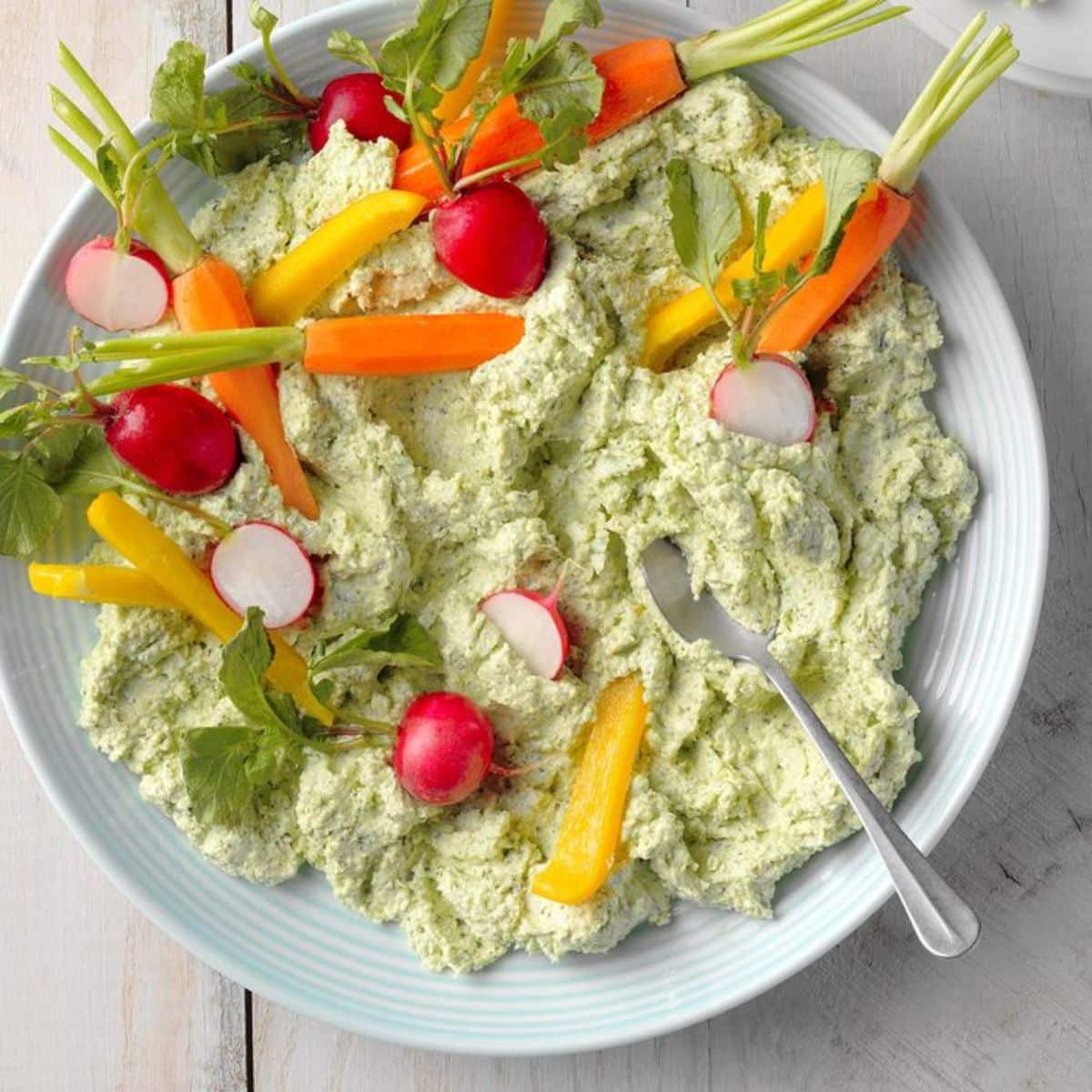 Herbed Feta Dip on a blue plate with a spoon and sliced veggies.