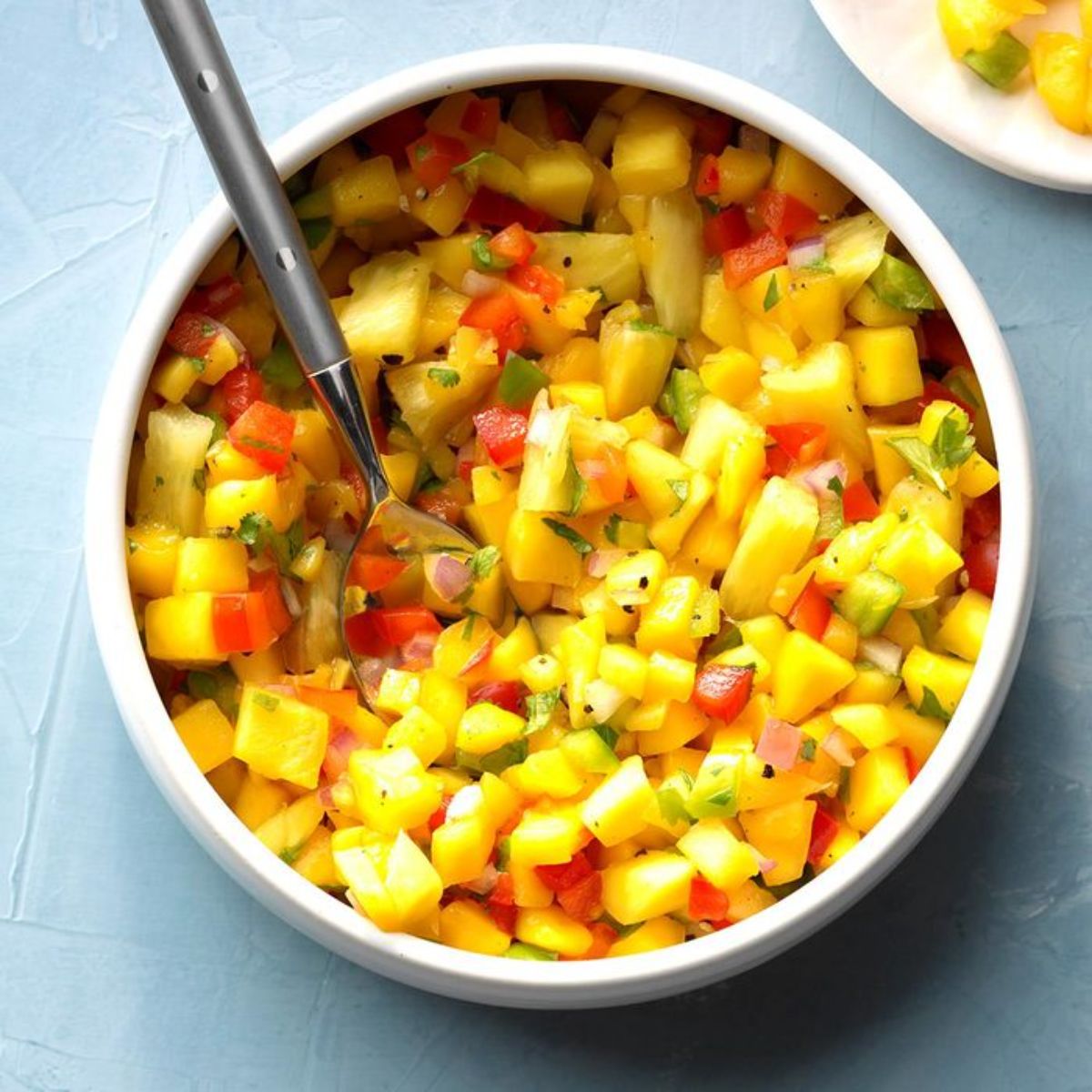 Pepper Mango Salsa in a white bowl with a spoon.