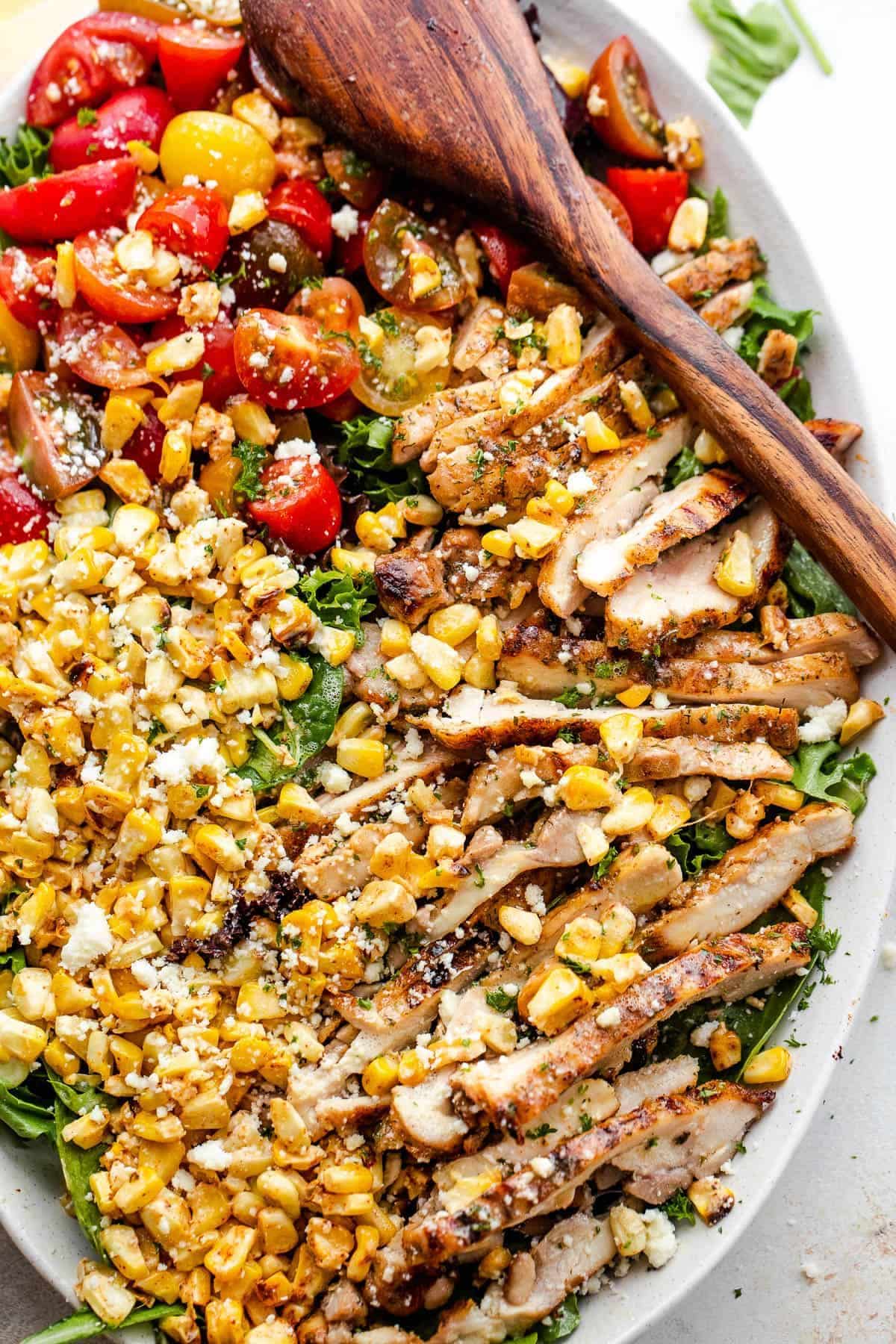 Mexican Street Corn Salad with Grilled Chicken on a white tray with a wooden spoon.