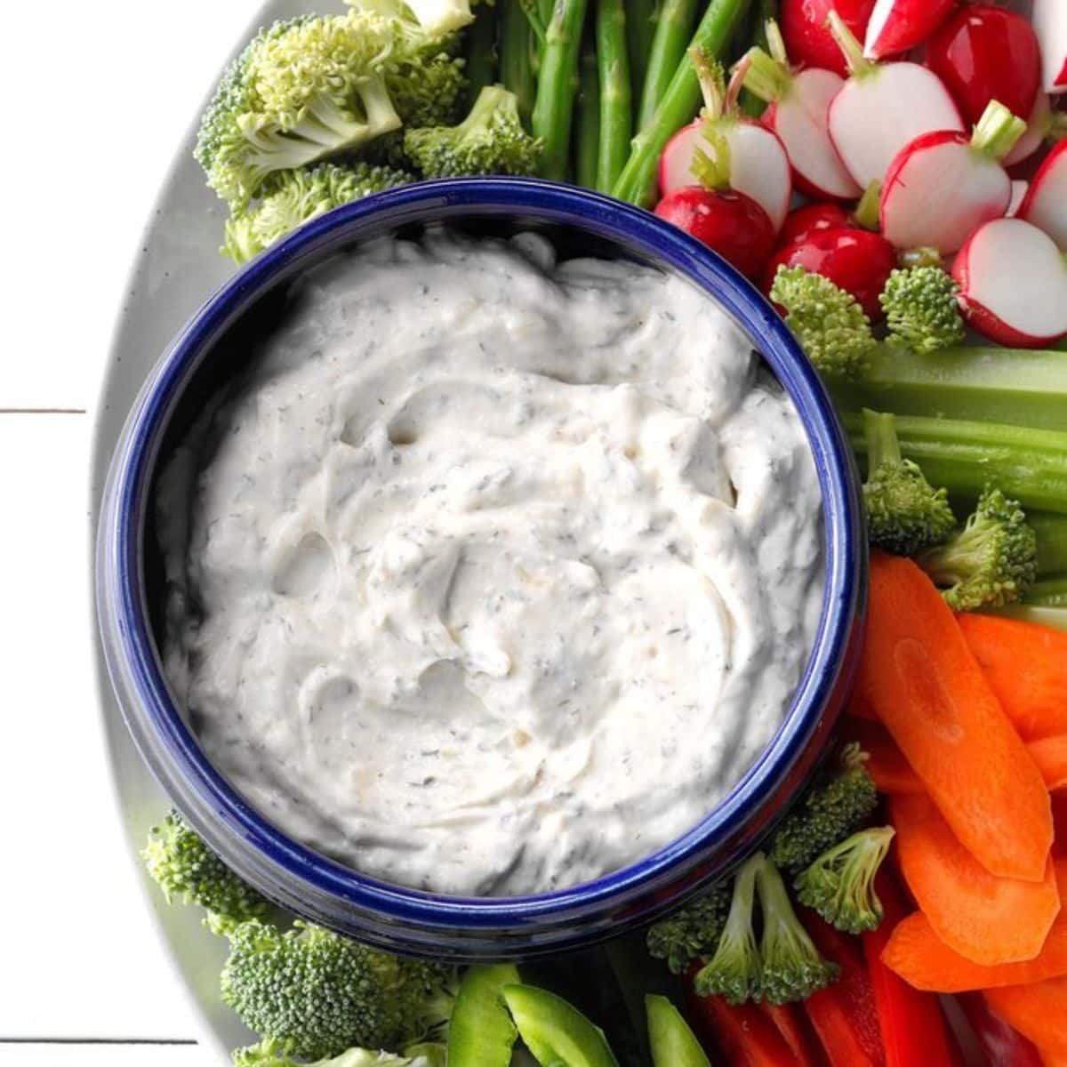 Veggie Dill Dip in a blue bowl on a tray with sliced veggies.