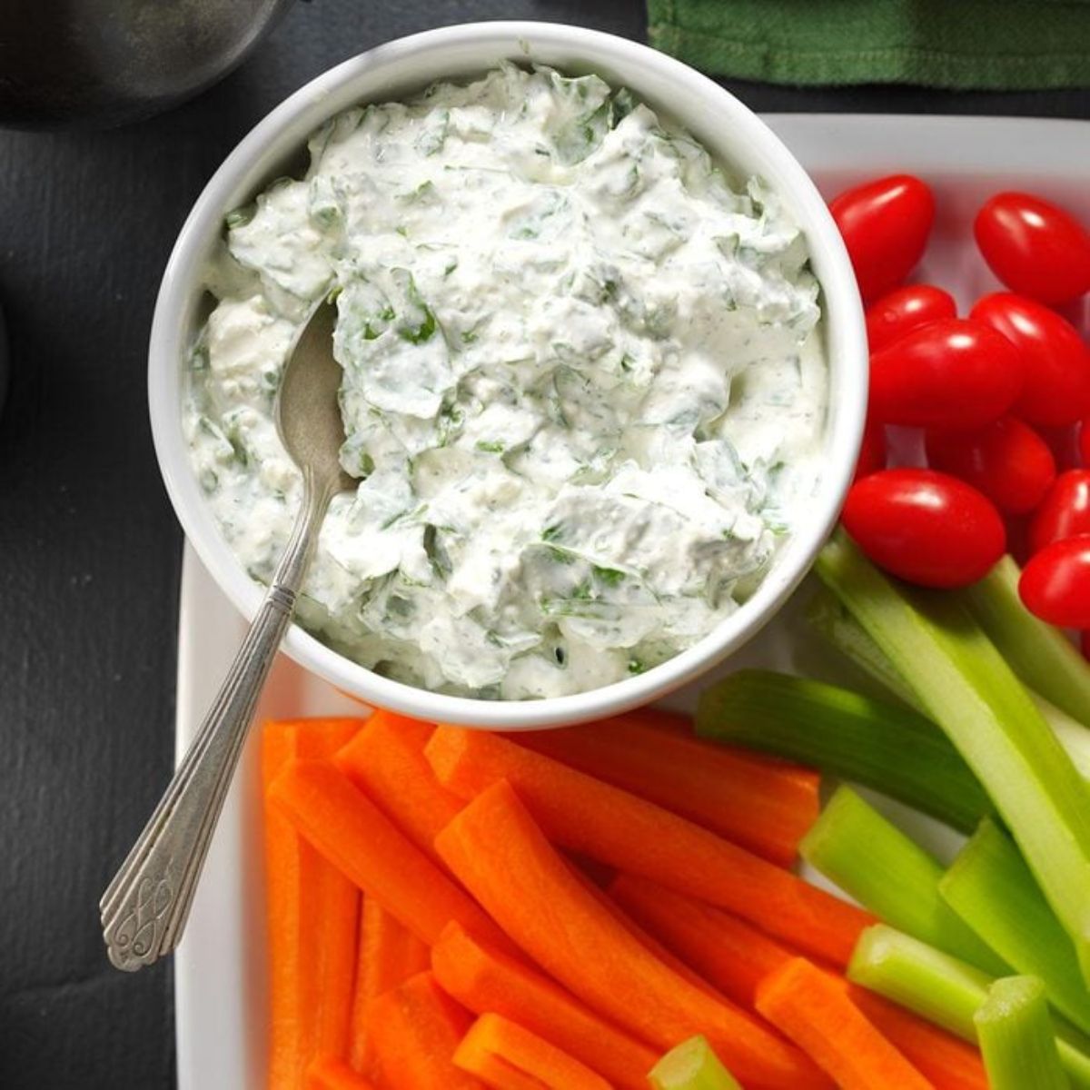Creamy Feta Spinach Dip in a white bowl with a spoon on a tray with sliced veggies.
