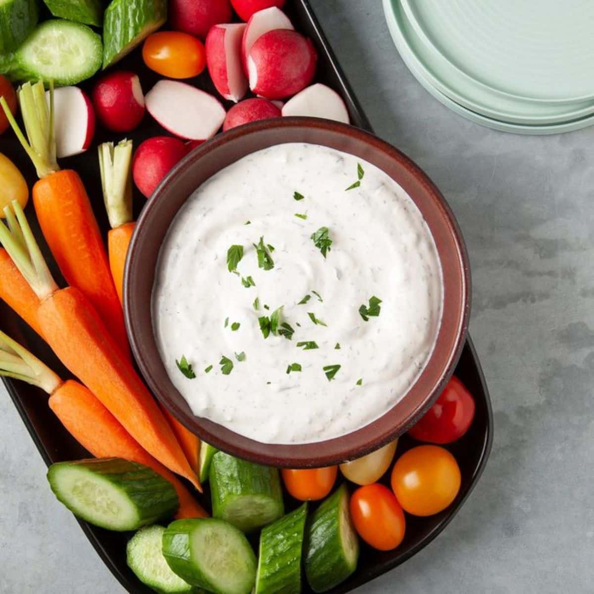 Crudite Dip in a brown bowl on a tray with sliced veggies.