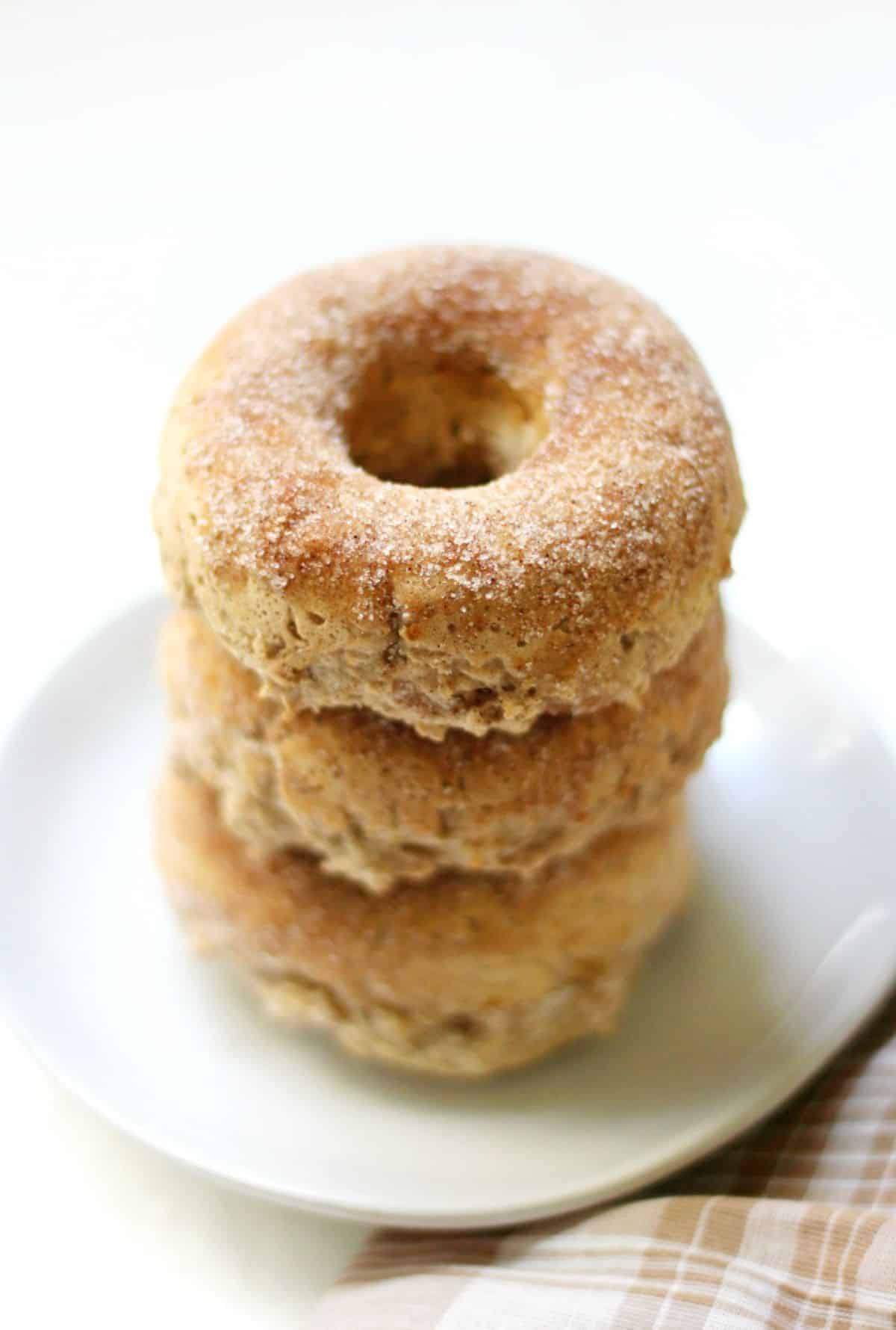 A pile of Baked Gluten-Free Apple Cider Doughnuts on a white plate.