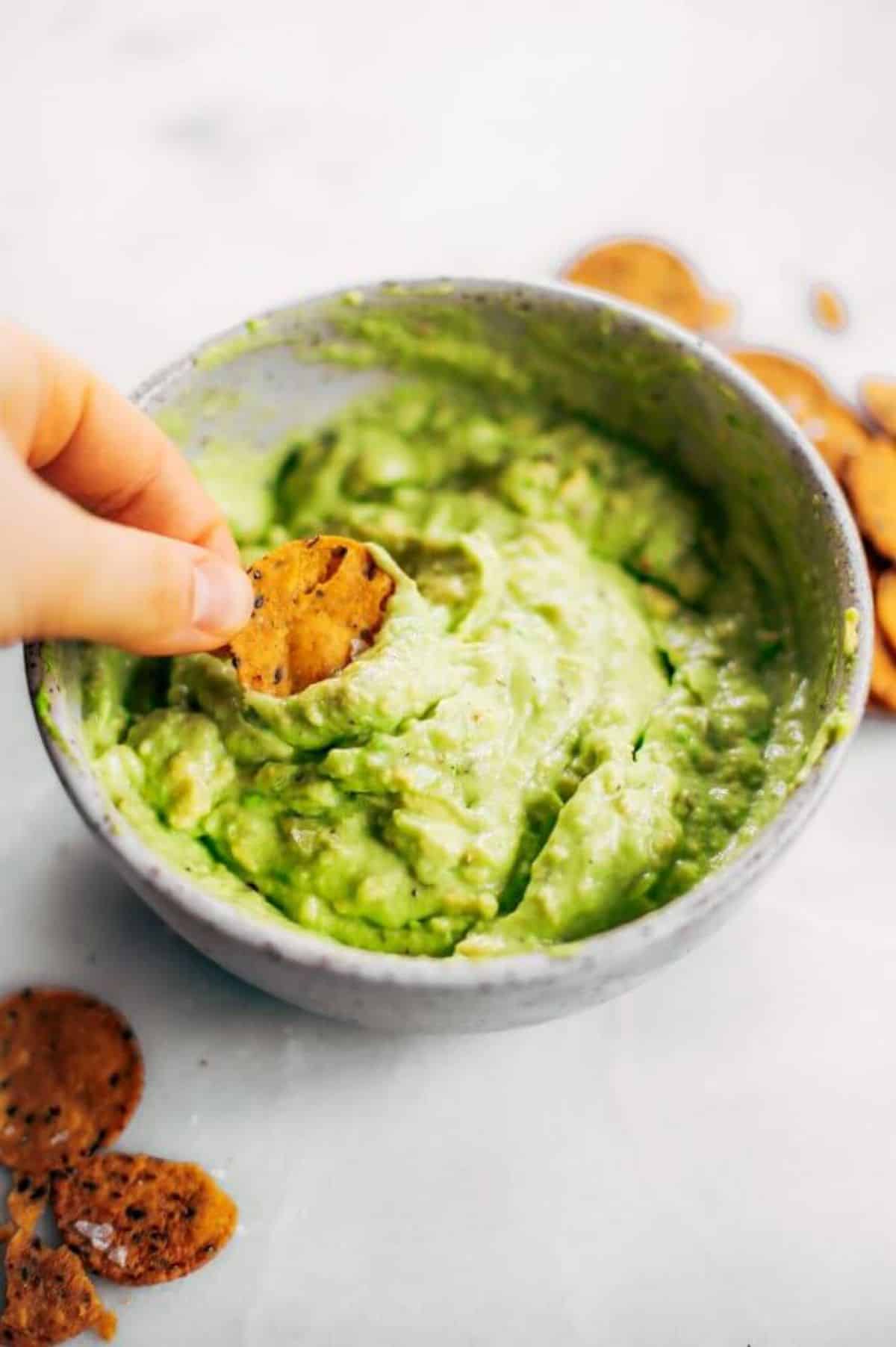 A cracker dipped in Avocado Lime Dip in a gray bowl.