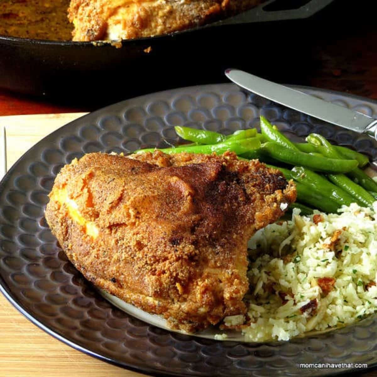 Crispy Cinnamon Chicken with rice and asparagus on a black plate.