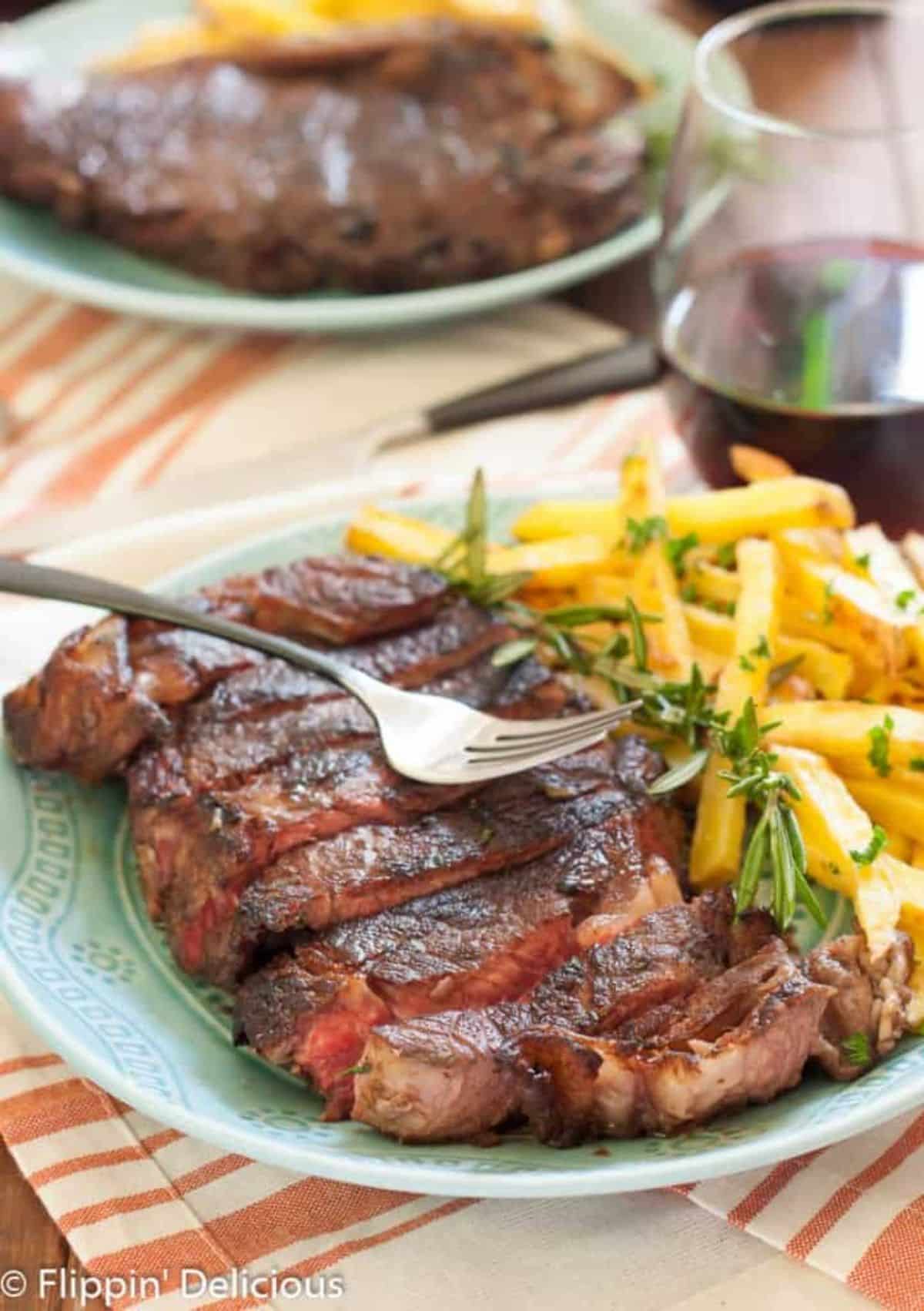 Red Wine-Marinated Steak with fries on a blue plate with a fork.