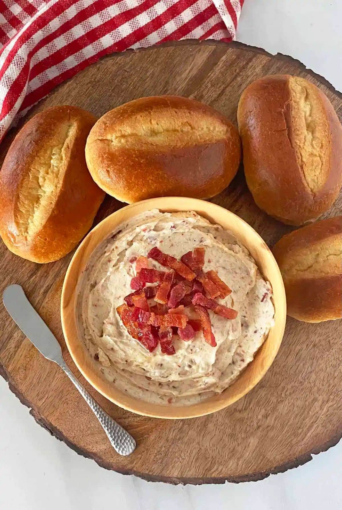 A bowl of Bacon Butter on a wooden tray with a knife and loafs of bread.
