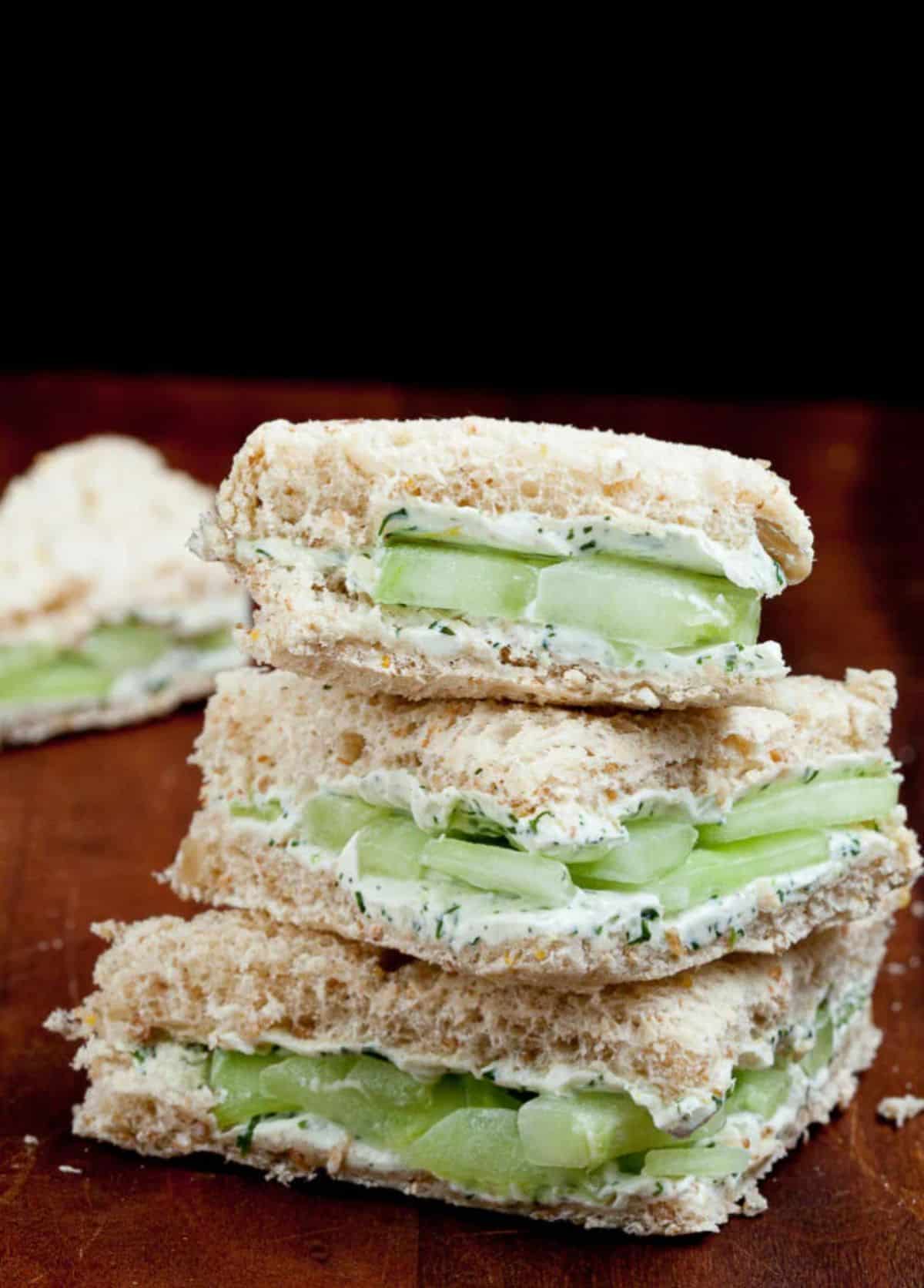 A pile of Cucumber Sandwiches with Cream Cheese & Lemon on a table.