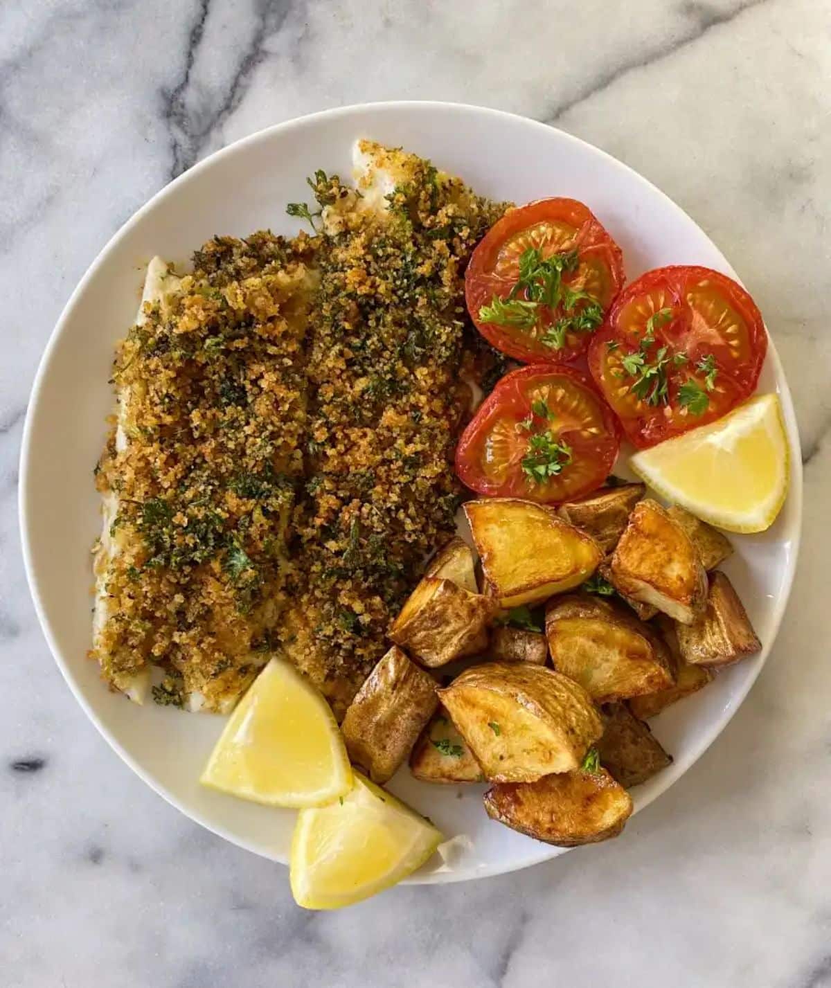 Crispy Baked Fish with Lemony Herbed Breadcrumbs with potatoes, tomatoes on a white plate.