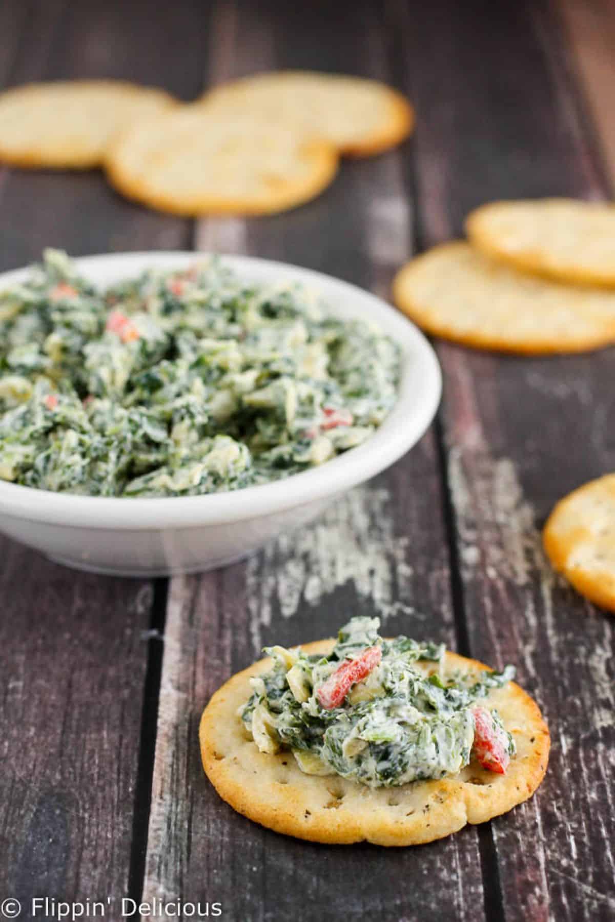 Delicious Gluten-Free Skinny Spinach Artichoke Dip in a white bowl and on cracker.