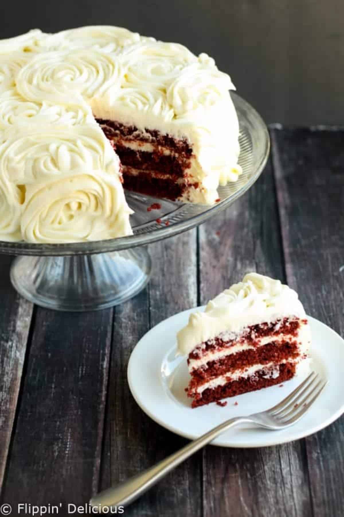 Delicious Red Velvet Cake on a glass cake tray and piece of cake on a white plate with a fork.