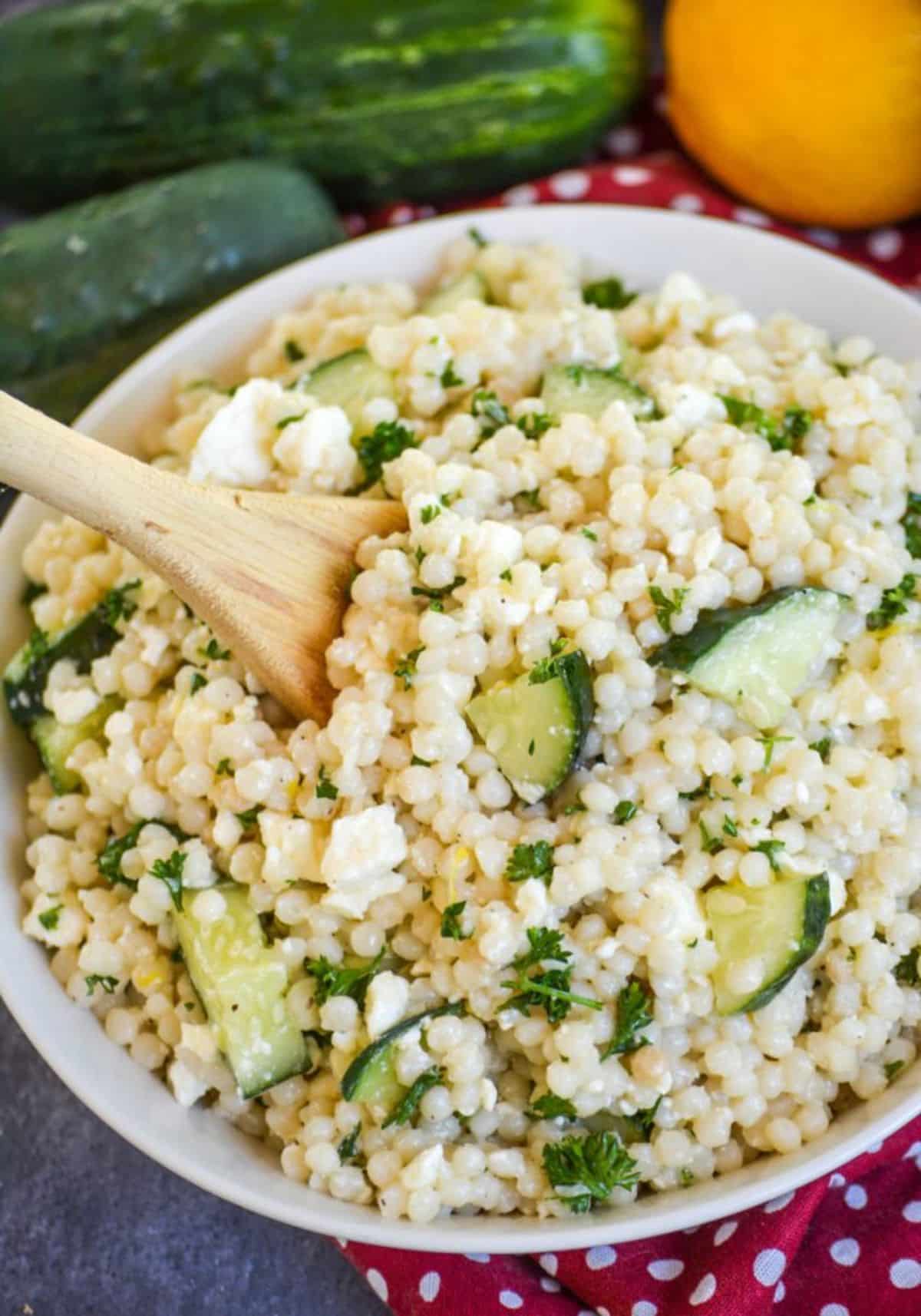 Flavorful Lemon Cucumber Couscous Salad in a white bowl with a wooden spoon.