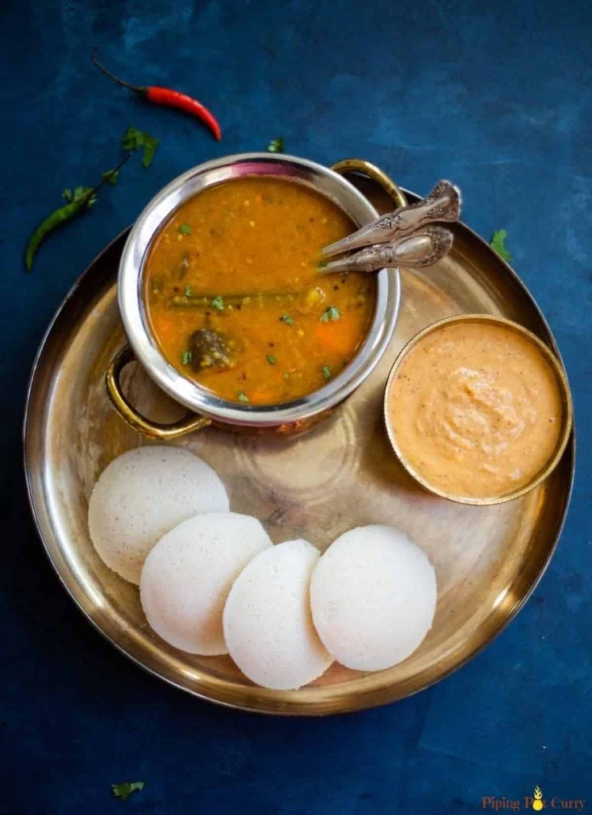 Crispy Steamed Idli - Savory Rice Cakes with a bowl of soup and a bowl of dip on a metal tray.