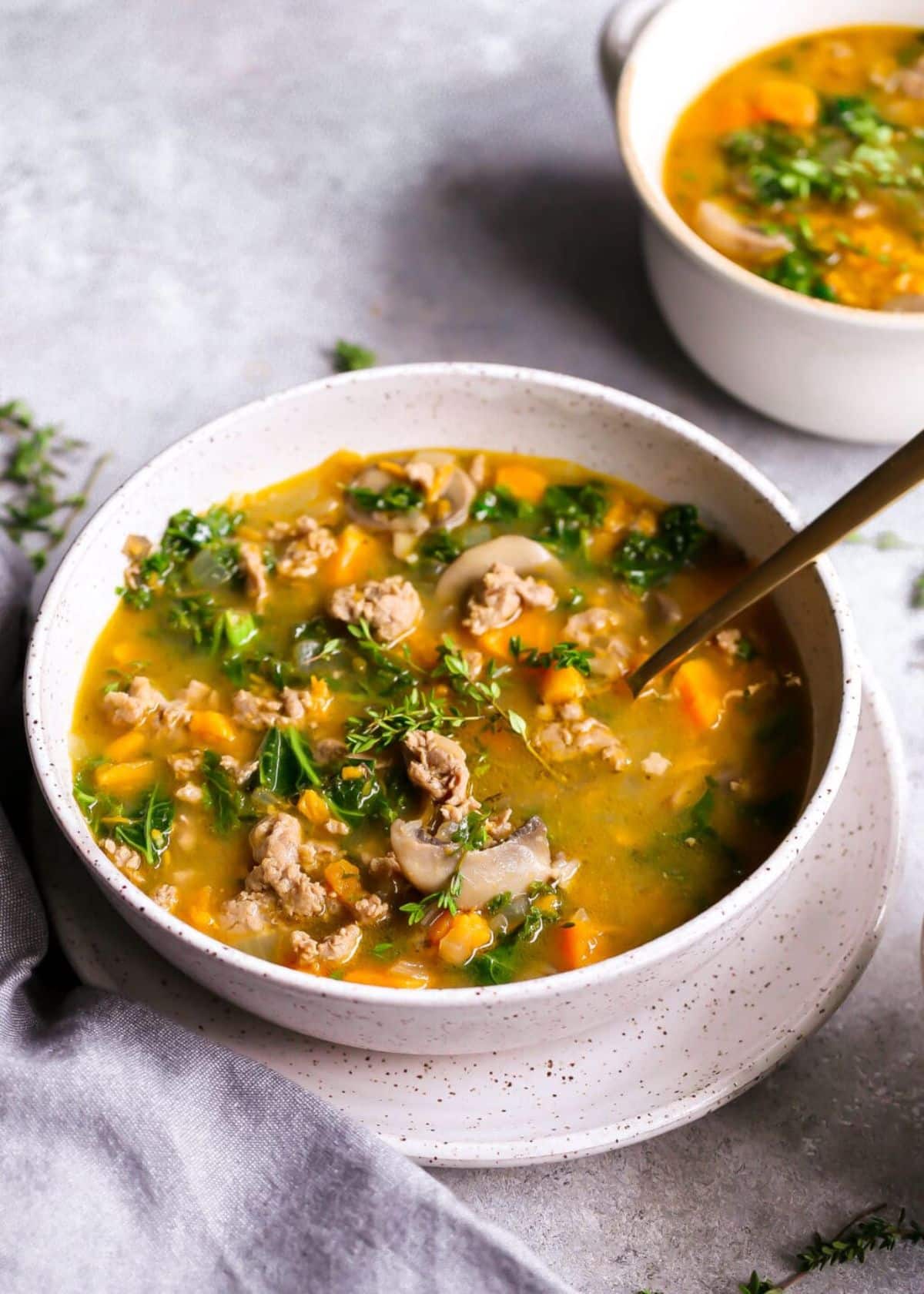 Delicious Sausage, Kale, and Sweet Potato Soup in a white bowl with a spoon.