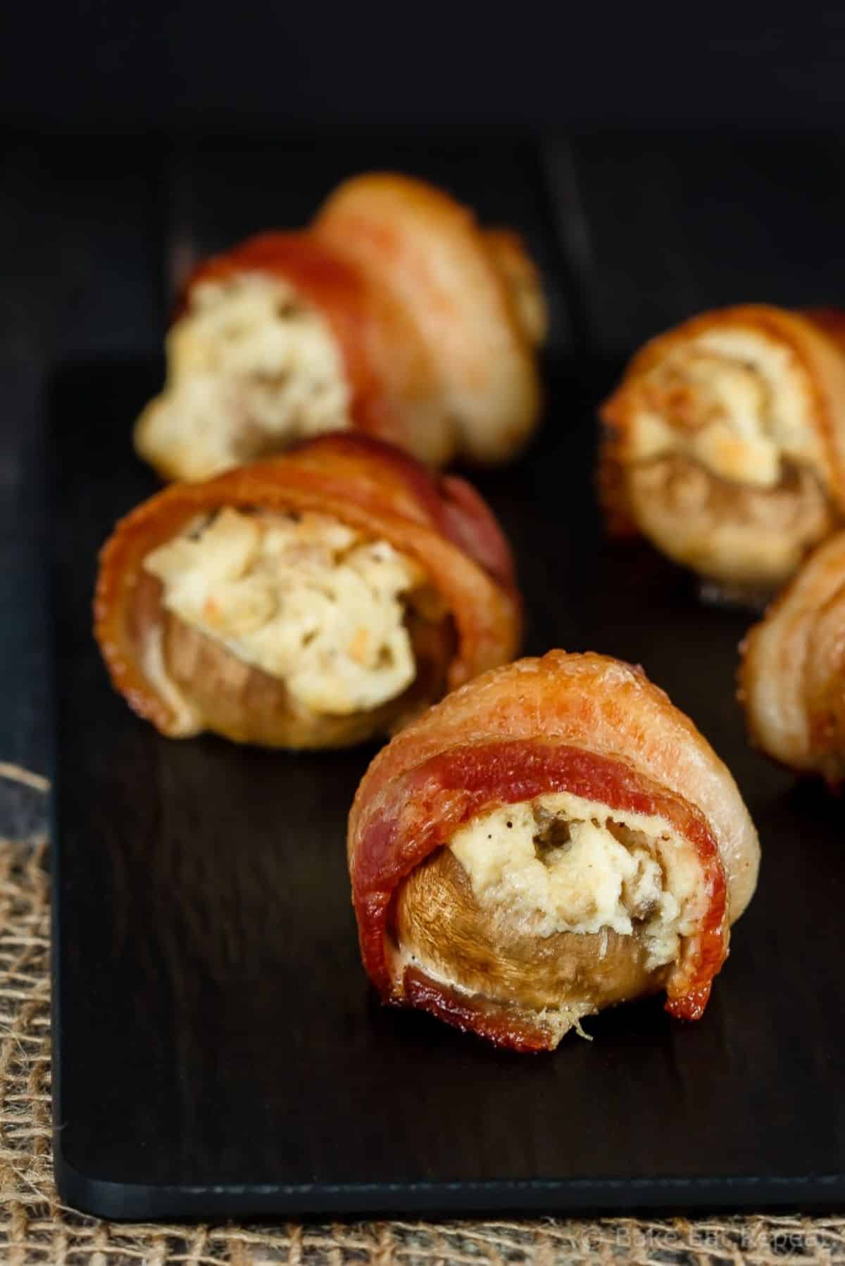 Scrumptious Bacon-Wrapped Crab-Stuffed Mushrooms on a black tray.