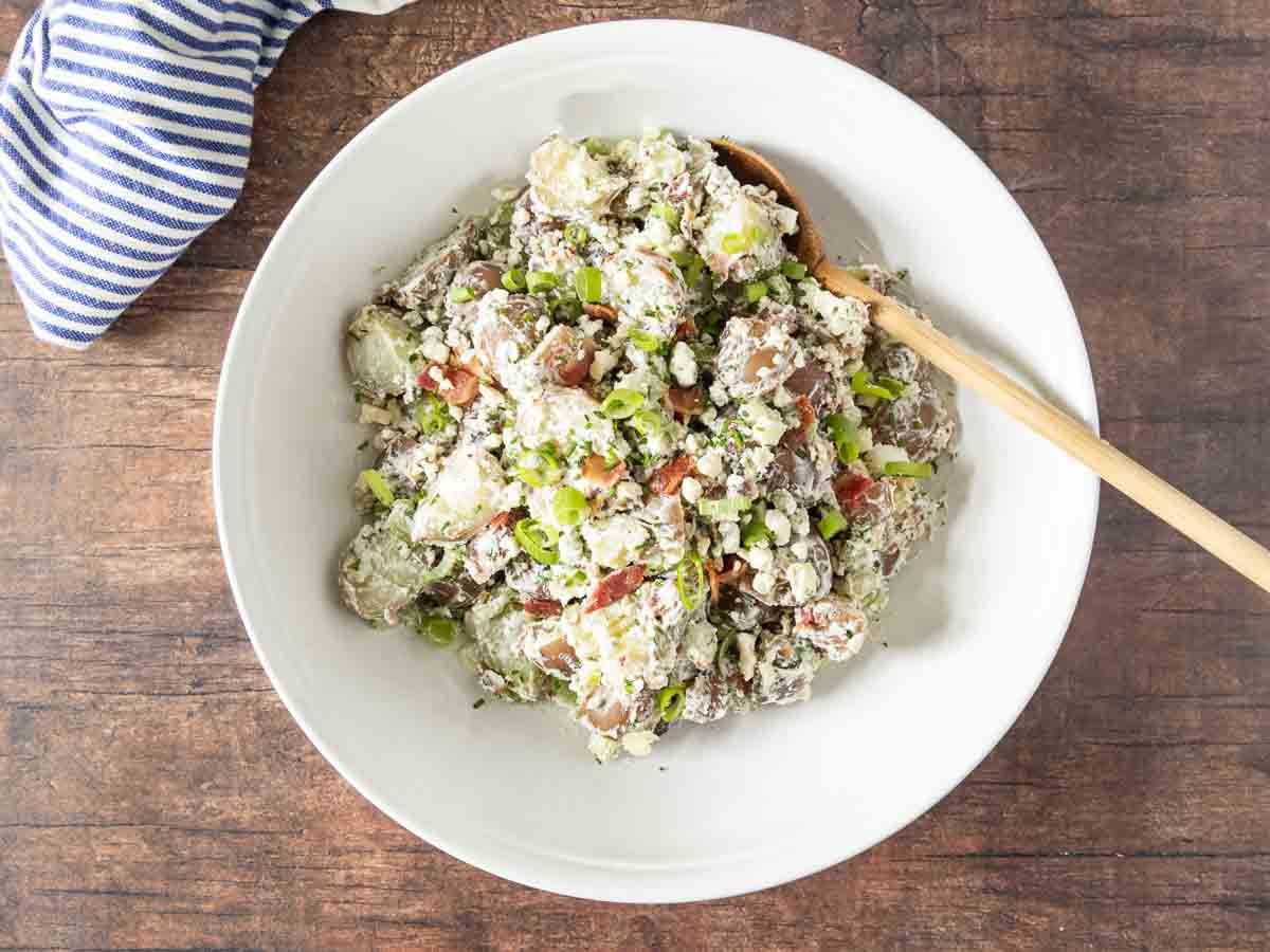 Healthy gluten-free Blue Cheese Potato Salad in a white bowl with a wooden spoon.