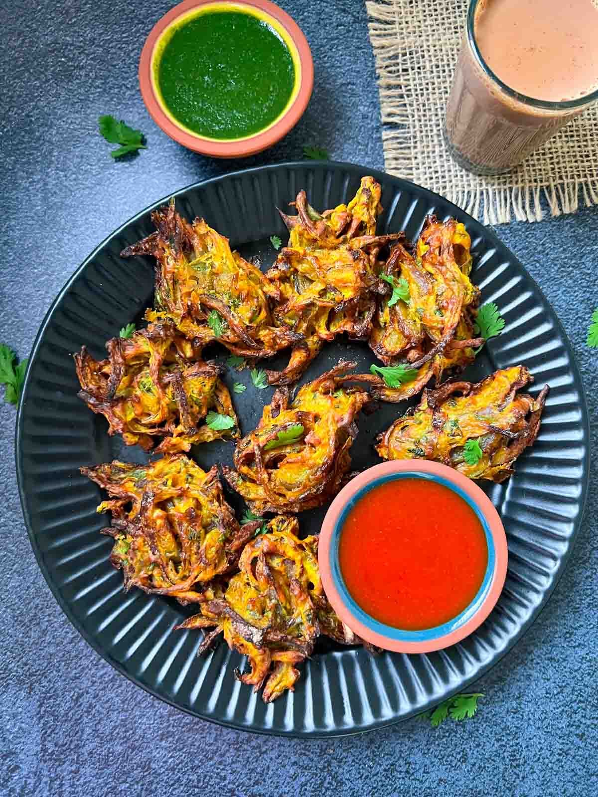 Scrumptious Onion Pakodas with a bowl of dip on a black plate.