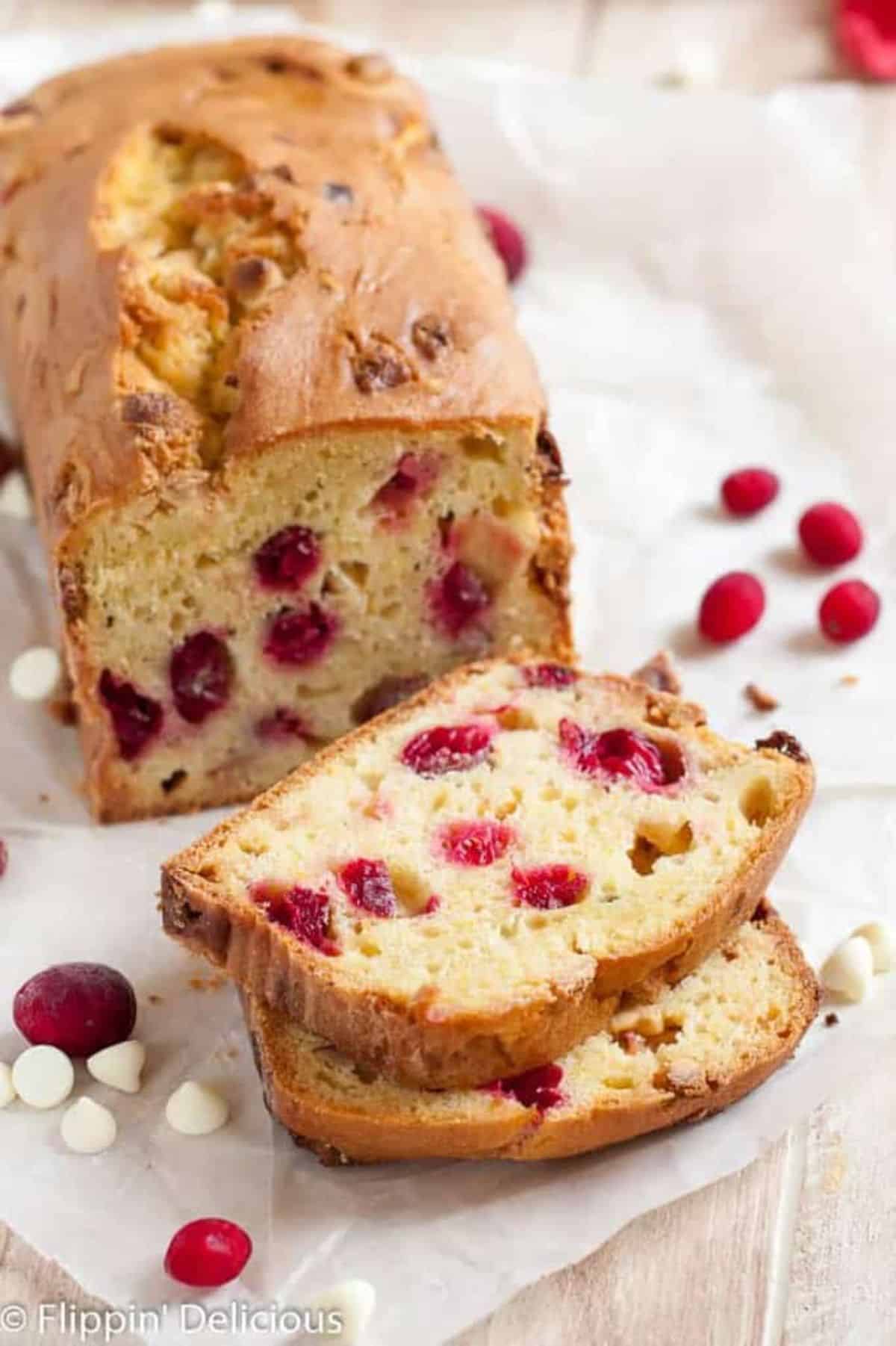 Partially sliced Gluten-Free Cranberry Bread with Orange, White Chocolate, and Hazelnuts on a table.