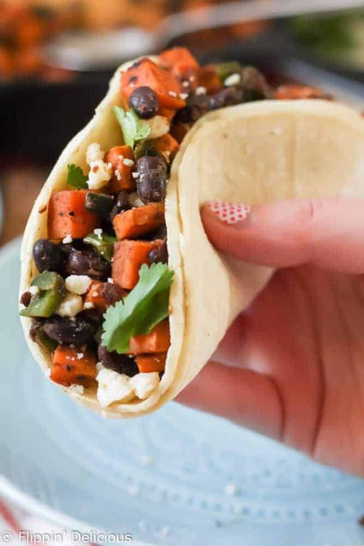 Mouth-watering Sweet Potato and Black Bean Vegetarian Tacos held by hand.