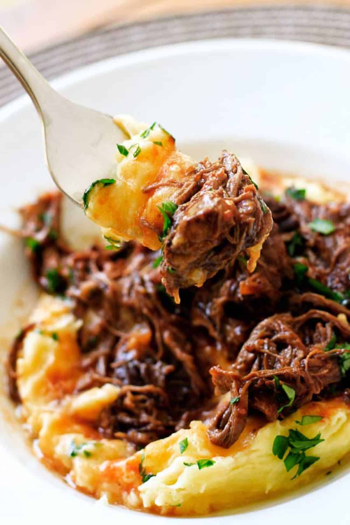 Mouth-watering Short Rib Ragu on a fork and on a white plate.