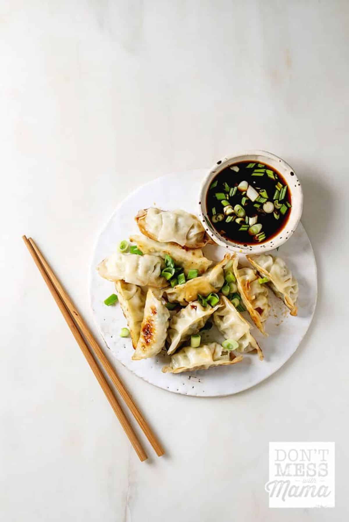 Delicious Chinese Dumplings with a bowl of dip on a plate.