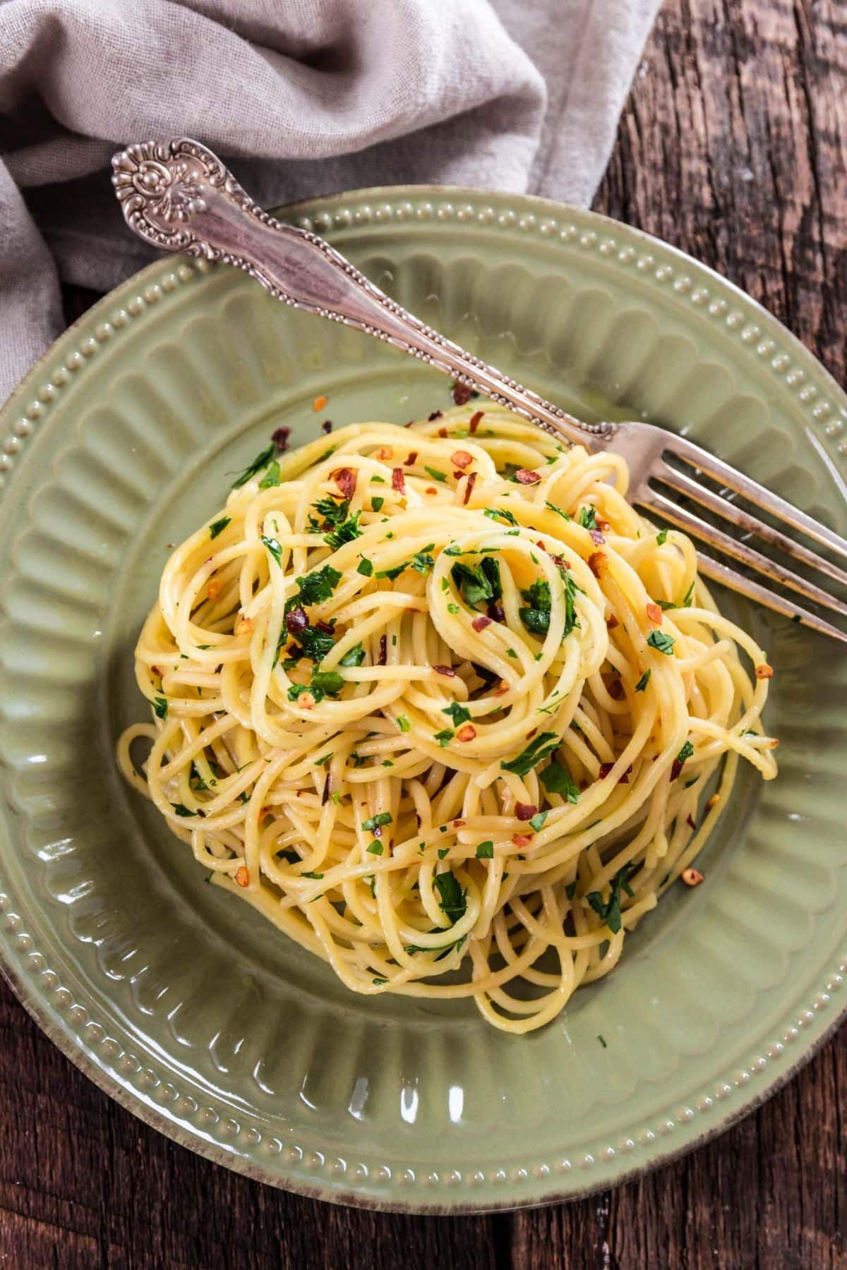 Healthy Spaghetti Aglio Olio e Peperoncino on a green plate with a fork.