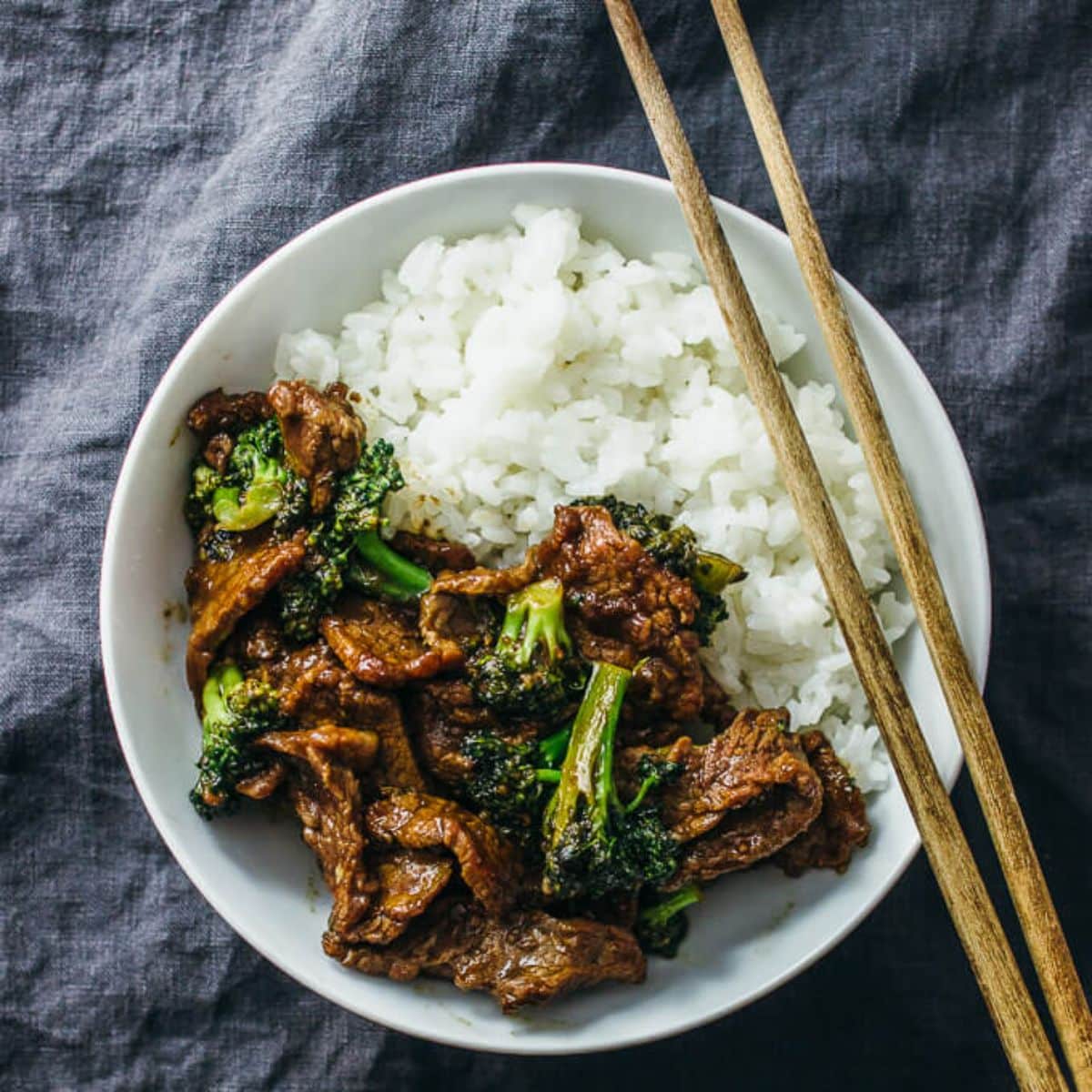 Healthy Beef And Broccoli with rice in a white plate with wooden chopsticks.
