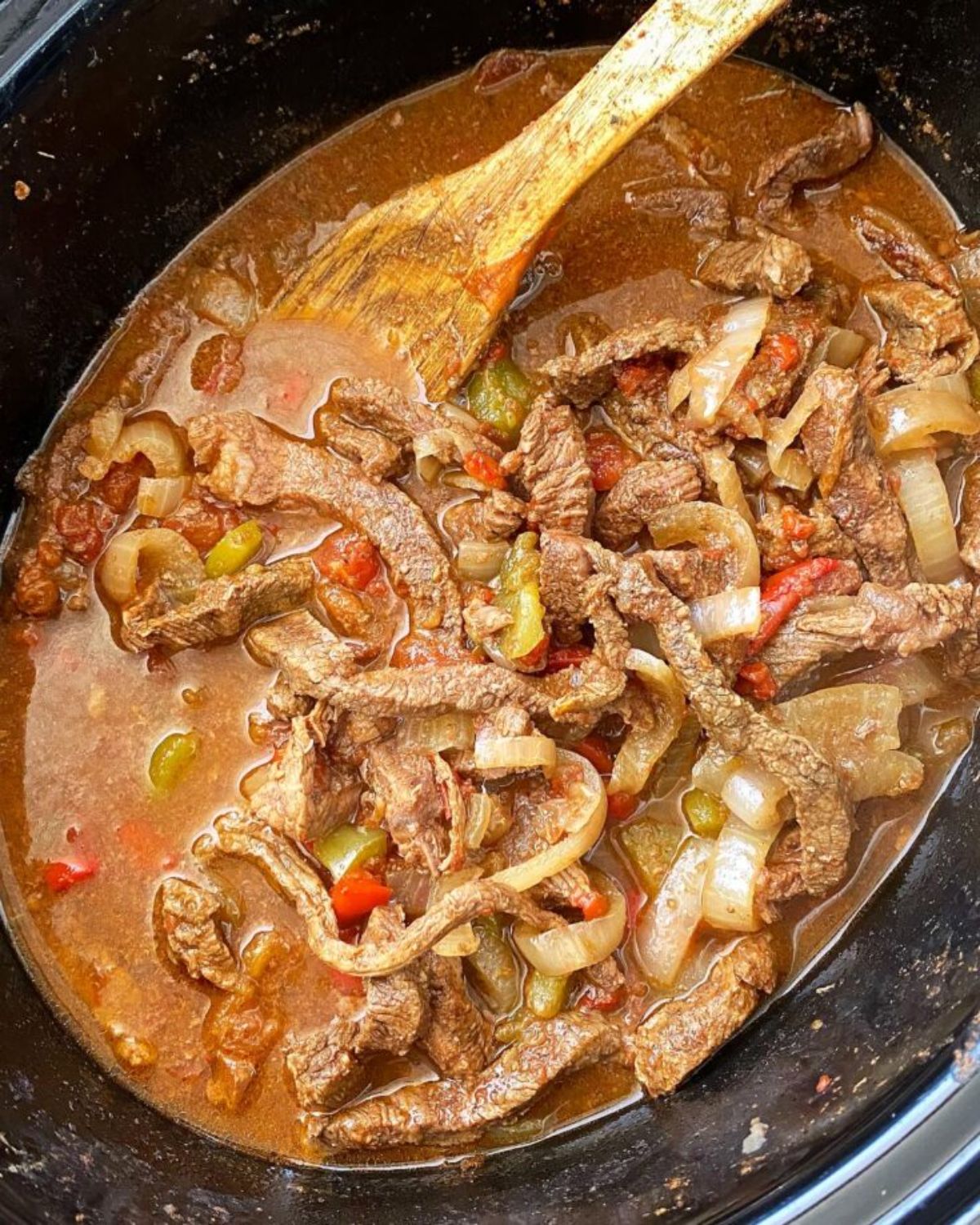 Juicy Slow Cooker Steak Fajitas in a pot with a wooden spoon.