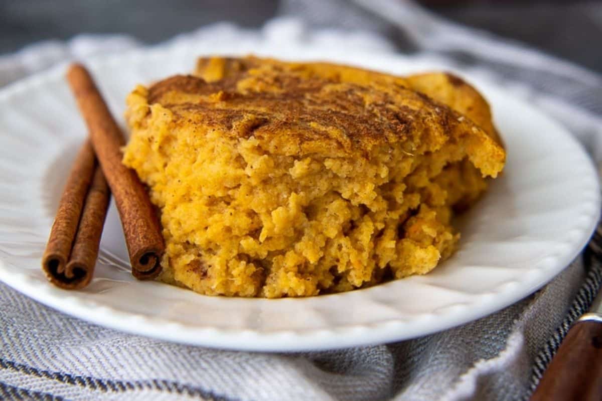 A piece of Southern Spoon Bread on a white plate with cinnamon sticks.