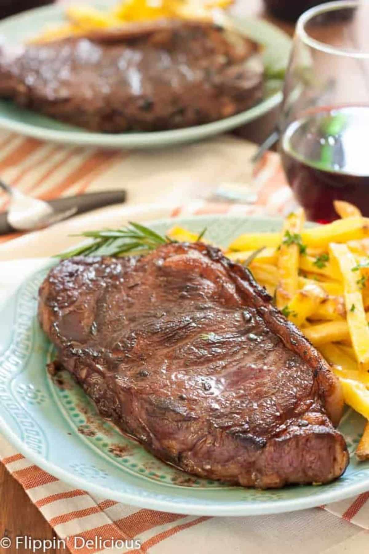 Scrumptious Red Wine Marinated Steak with Baked Garlic and Herb Fries on a green plate.