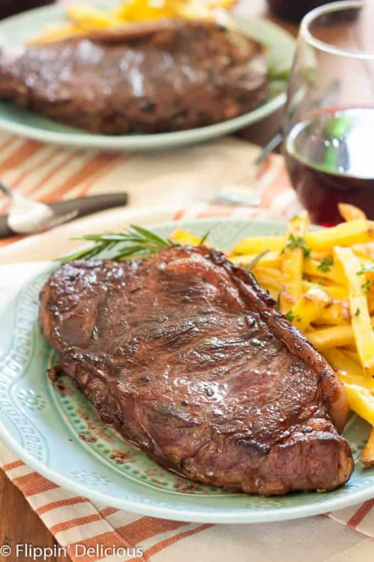 Juicy Red Wine Marinated Steak with Baked Garlic and Herb Frieson a blue plate.