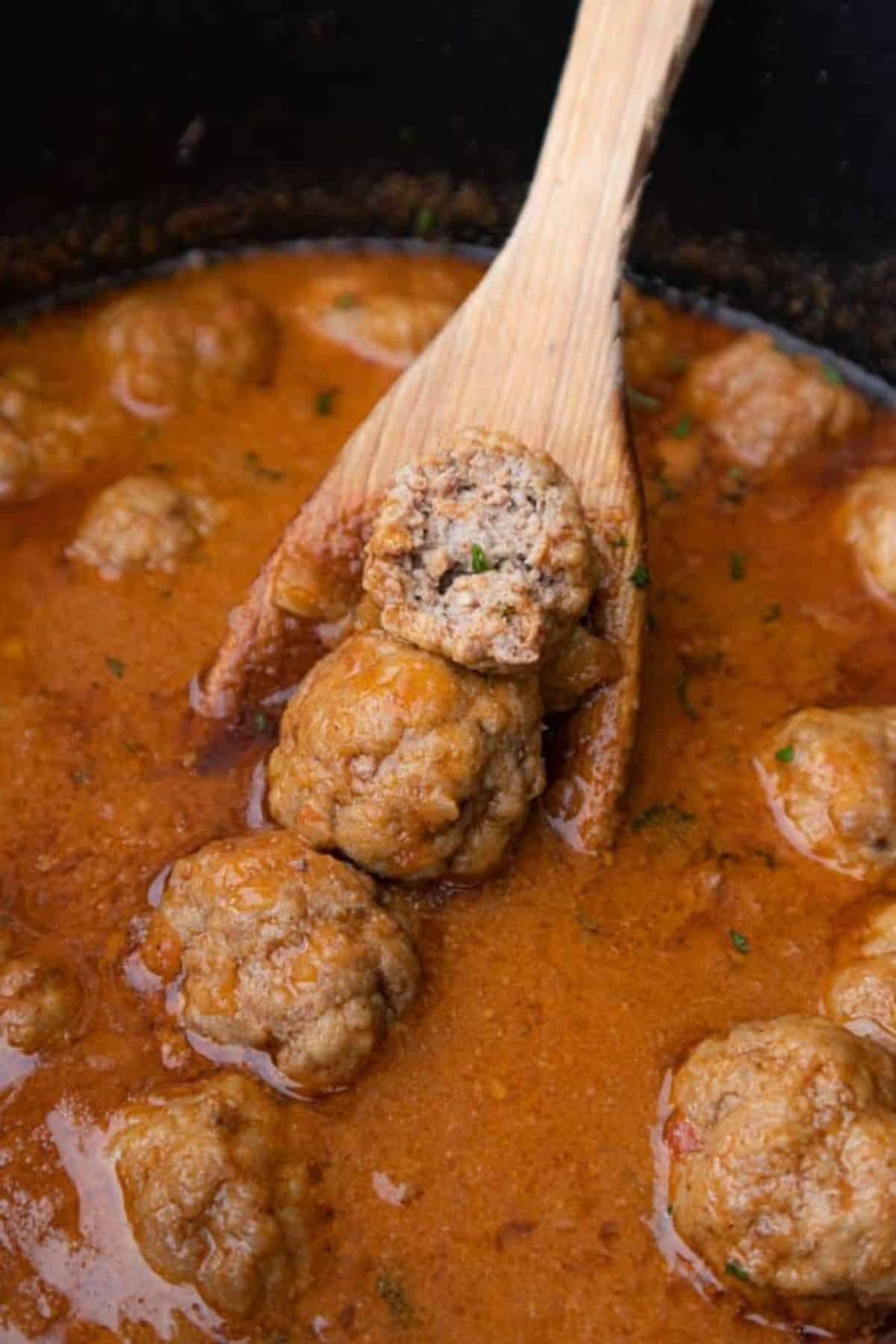 Delicious Gluten-Free Spanish Meatballs in a pot stirred with a wooden spatula.