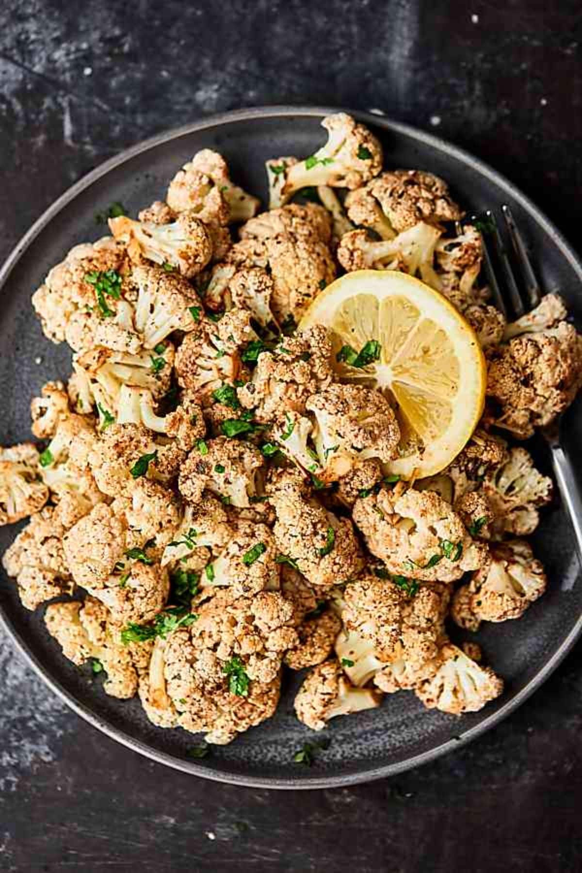 Delicious gluten-free Mediterranean Cauliflower on a black plate with a fork.